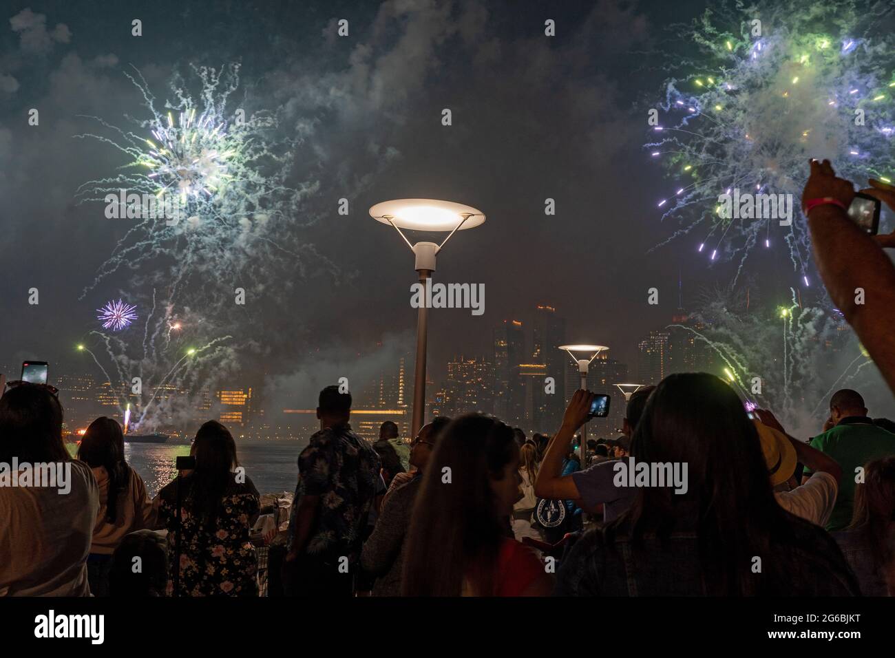NEW YORK, NY - JULI 04: Zuschauer beobachten das Feuerwerk während der 45. Jährlichen Macy's Feuerwerksschau am 4. Juli 2021 mit Blick auf die Skyline von Manhattan am Gantry State Plaza in Long Island City im Stadtteil Queens von New York City. Als Beweis für die Verbesserung der Stadt gegenüber COVID-19 war die diesjährige Feier mit einer Laufzeit von 25 Minuten größer und länger als in den Vorjahren geplant. Aufgrund der Coronavirus-Pandemie des vergangenen Jahres wurde das Feuerwerk über vier Nächte und mehrere Bezirke verteilt, um Versammlungen zu begrenzen und die Ausbreitung zu verlangsamen. Kredit: Ron Adar/Alamy Stockfoto
