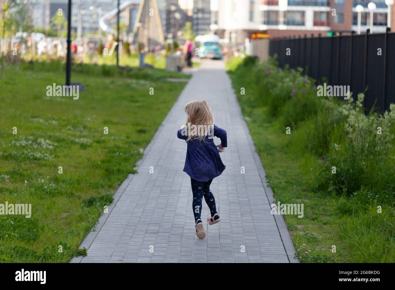 Ein Kind rennt im Park entlang der Straße vor dem Hintergrund eines Spielplatzes fort Stockfoto