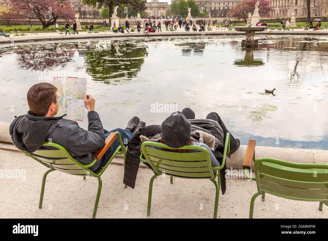 Zwei Touristen, die in ihren Stühlen schaukeln, sitzen am Rande eines Wasserkörpers im Garten der Tuilerien in Paris Stockfoto