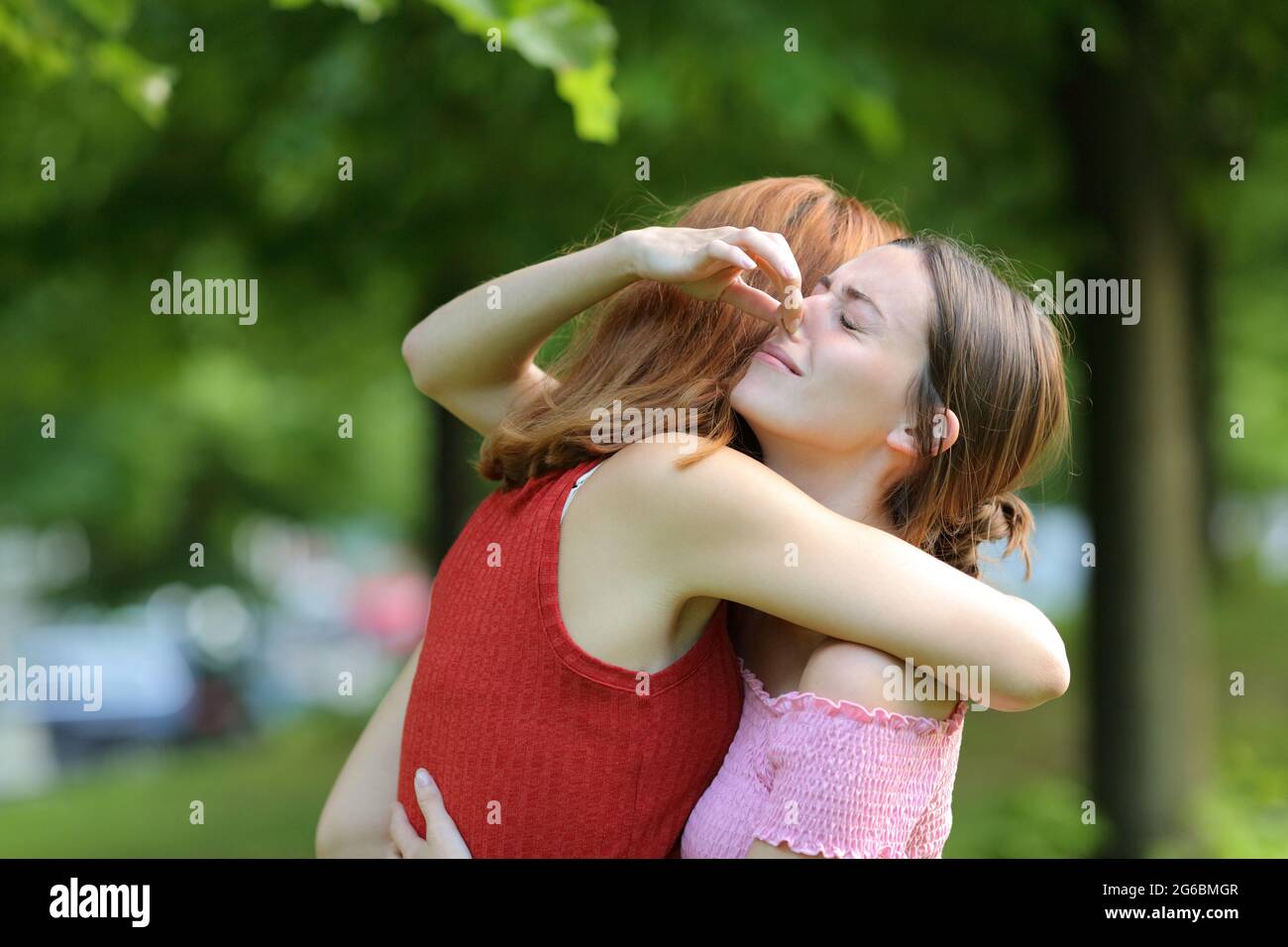 Frau umarmt ihre Freundin und hält ihre Nase, um schlechten Geruch in einem Park zu vermeiden Stockfoto