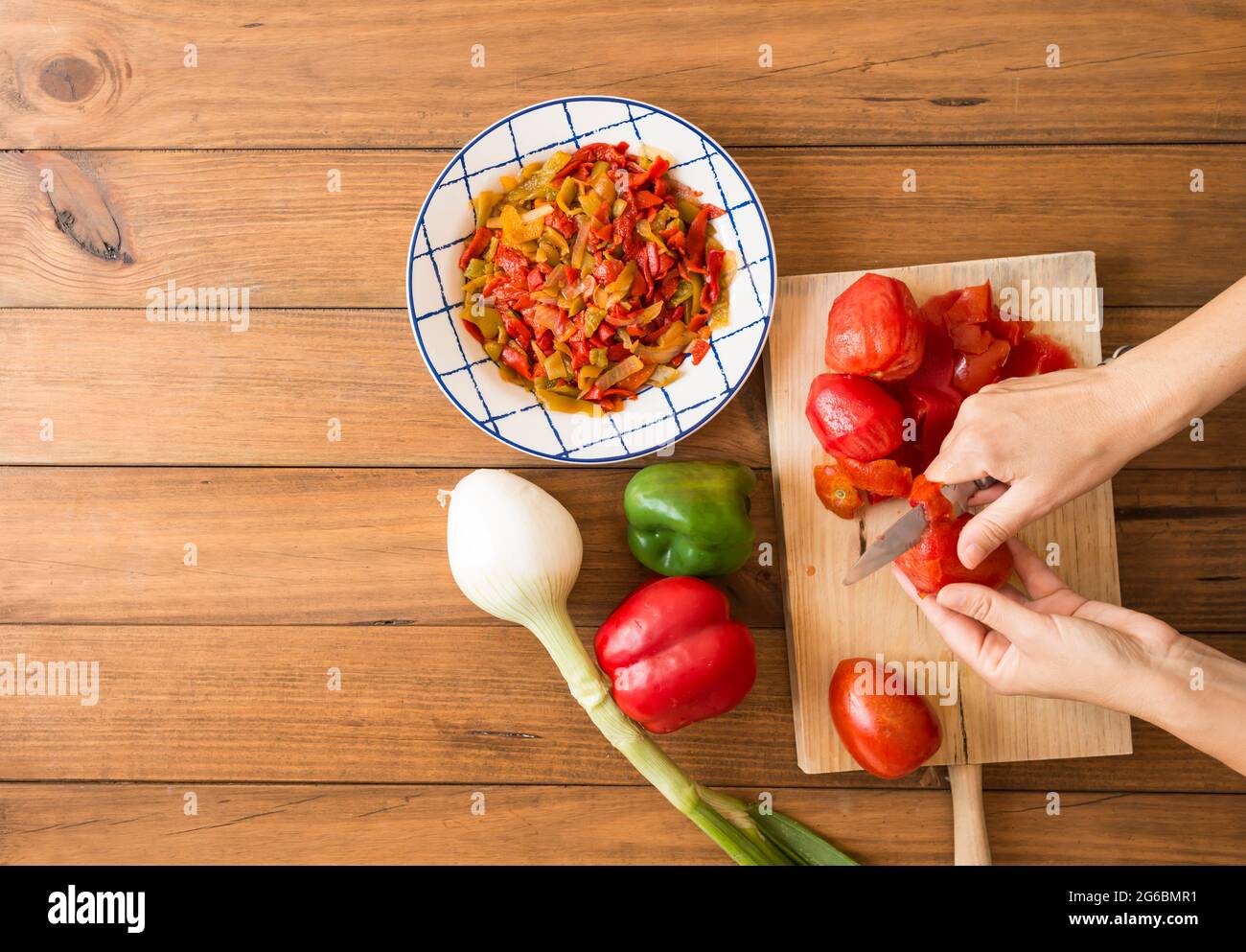 Detail der Hände einer Frau, die Tomaten mit einem Messer schält. Zubereitung von gerösteten Paprika, einem typischen Gericht der spanischen und andalusischen Küche. Stockfoto