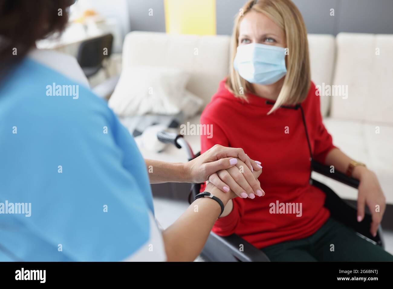 Arzt hält die Hand einer behinderten Frau im Rollstuhl in einer schützenden medizinischen Maske Stockfoto
