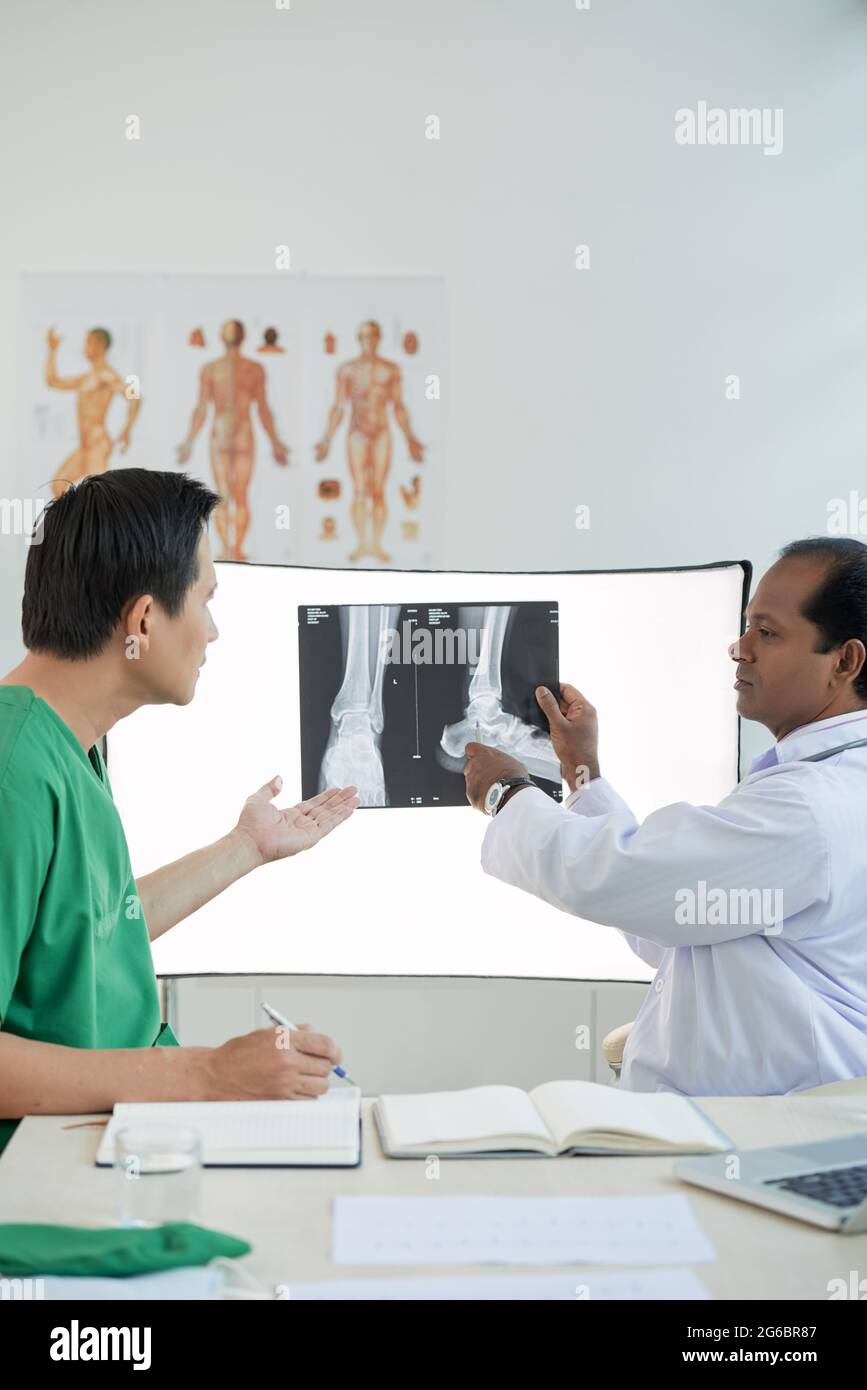 Chirurg und Radiologe diskutieren die Behandlung von Fersenfrakturen und zeigen auf die Füße, das Röntgenbild an der Wand Stockfoto