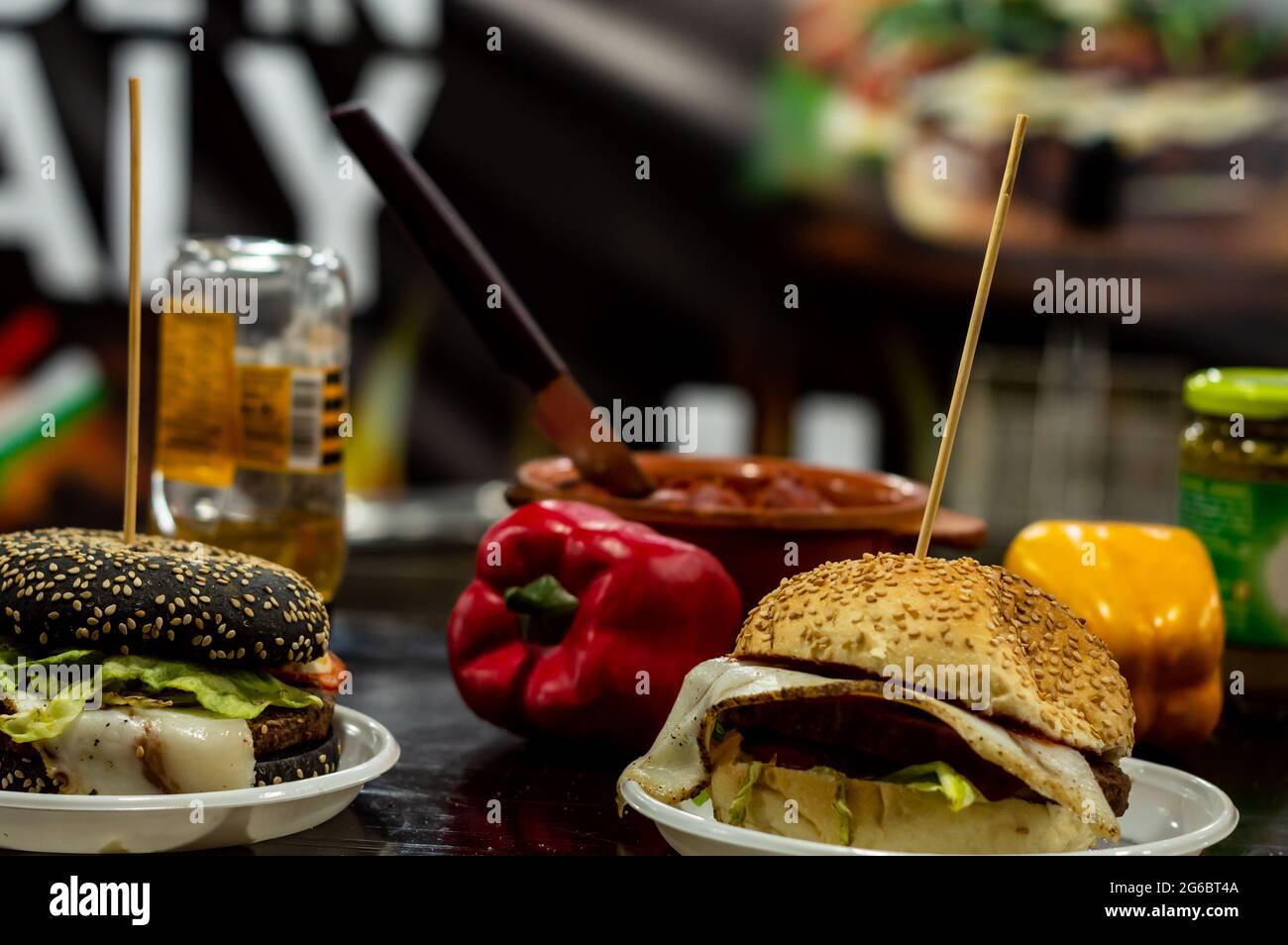 Zwei Käseburger auf einem Tisch mit roten und gelben Paprika im Hintergrund an der Lebensmitteltheke Stockfoto