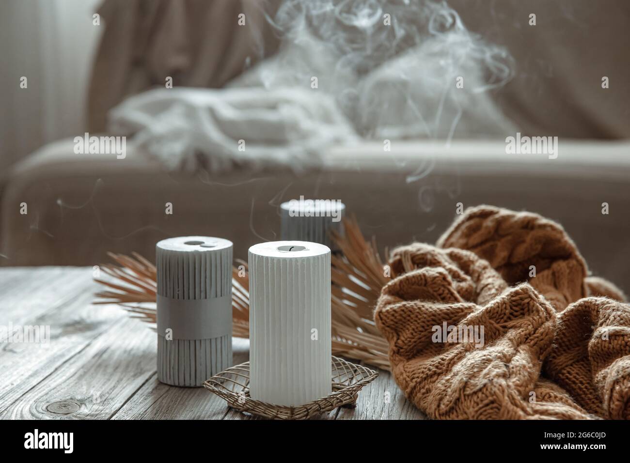 Gemütliche Wohnkomposition mit erloschenen Kerzen auf einem Holztisch mit gestricktem Element. Stockfoto