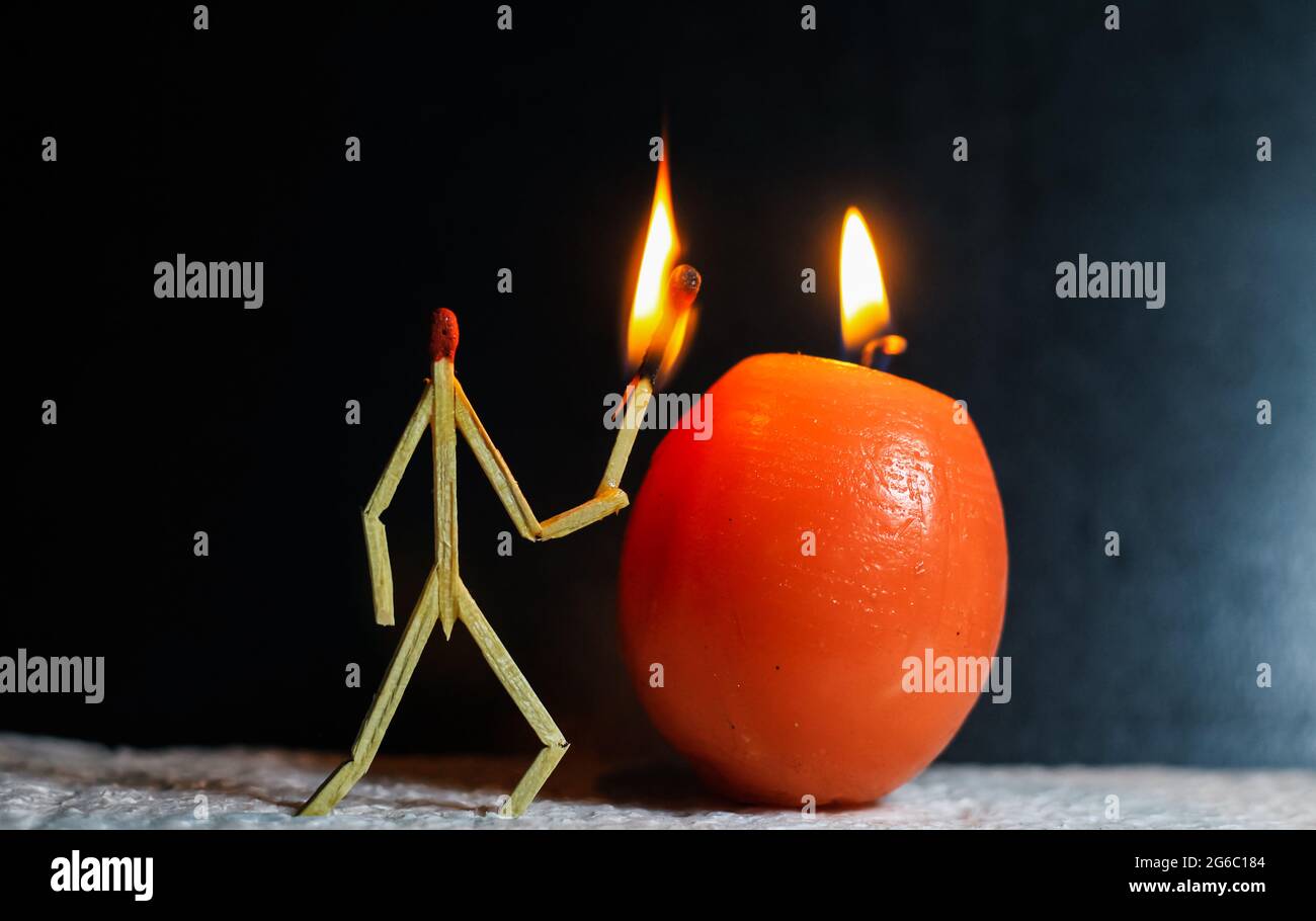 Streichhölzer in Form eines Mannes, der eine Kerze anzündet, Streichhölzer, der eine Kerze anzündet. Die Matchstick-Kunstfotografie verwendete Matchsticks, um den Charakter zu erschaffen. Stockfoto