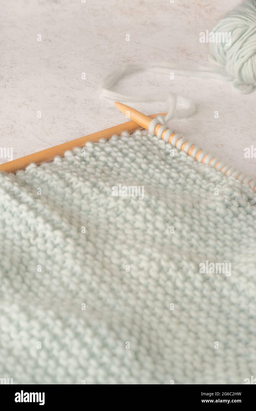Weicher Fokus leichter Strickhintergrund mit großen Holznadeln und mintfarbener Wolle auf einem Marmorhintergrund mit Kopierfläche Stockfoto