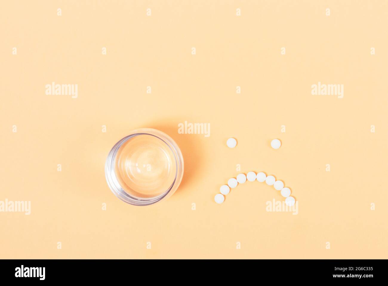 Schmerz- und Krankheitskonzept, Pillen in Form eines traurigen Smiley-Gesichts neben einem Glas Wasser auf einem beigen Tisch, Draufsicht. Stockfoto