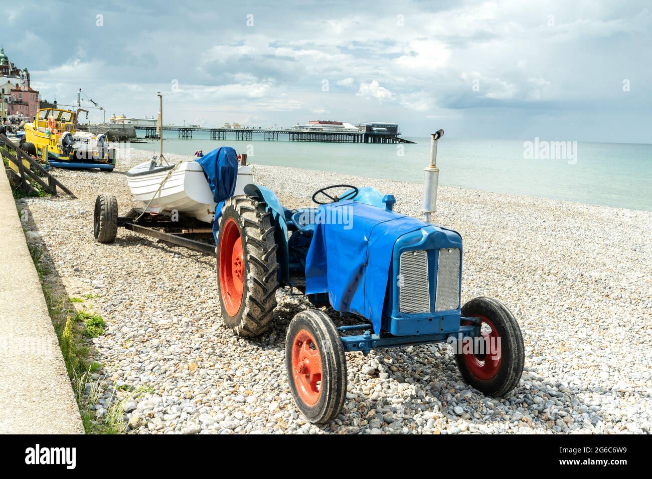 Blick auf Traktor und Fischerboot am Strand von Cromer im Norden von Norfolk, Großbritannien, mit berühmtem Pier im Hintergrund Stockfoto