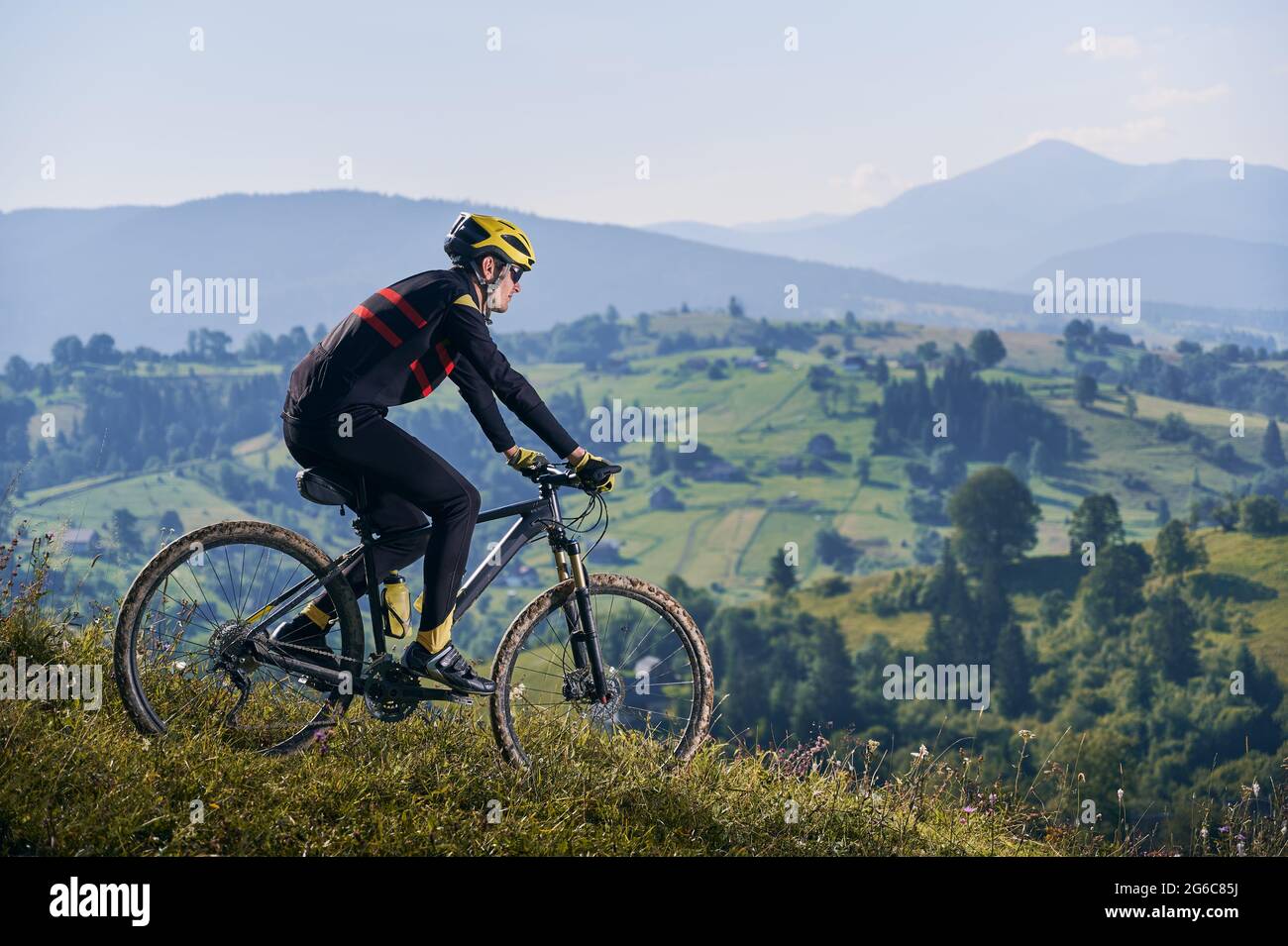 Horizontale Momentaufnahme eines Mannes, der am frühen nebligen Morgen mit seinem Fahrrad in den Bergen fährt und bergab fährt. Gipfel in Wolken, grüne Hügel im Hintergrund. Seitenansicht, Kopierbereich. Konzept des aktiven Lebensstils Stockfoto