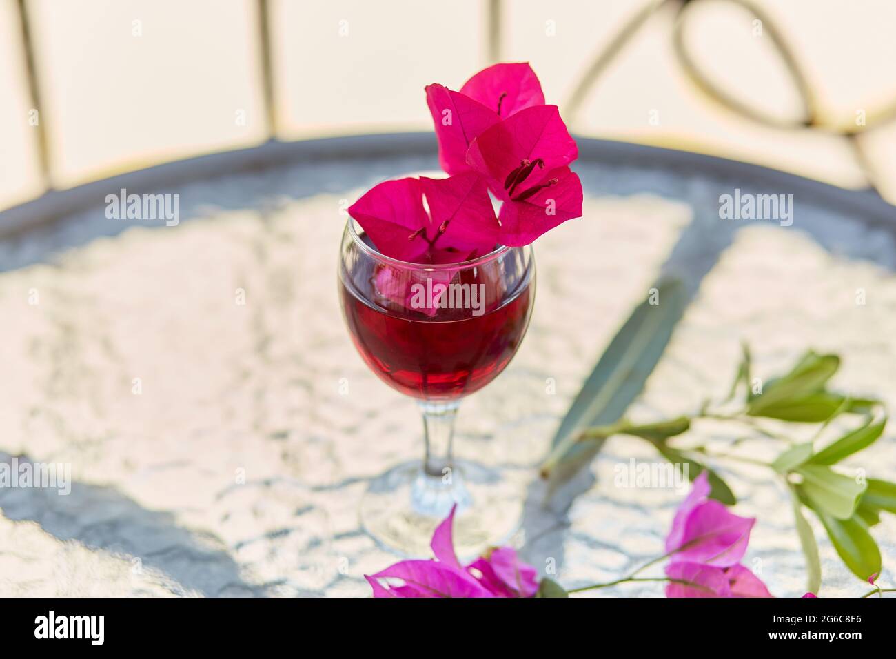 Rosafarbene, surreale tropische Blüten von Bougainvillea und ein Glas Rotwein. Festlicher Sommerhintergrund. Speicherplatz kopieren. Stockfoto