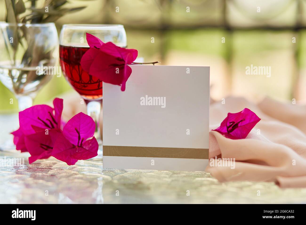 Elegantes Glas Rotwein. Dekorative rosa Blüten von Bougainvillea. Nachbau einer Postkarte oder Einladung. Festliches Weihnachtskonzept. Dekorative grüne Blätter und Zweig des Olivenbaums im Glas. Stockfoto