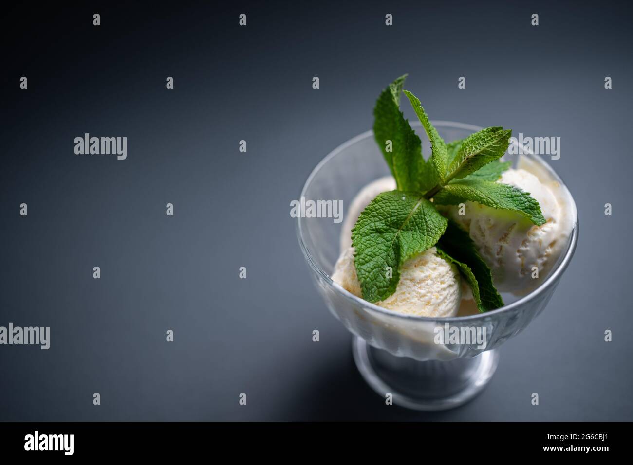 Leckeres Vanilleeis mit frischer Minze in Glasschüssel auf schwarzem Hintergrund Stockfoto