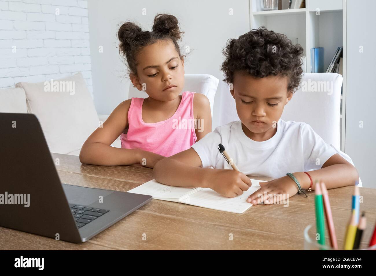 afroamerikanische ältere Schwester, die dem jüngeren Bruder bei Hausaufgaben am Schreibtisch zusieht Stockfoto