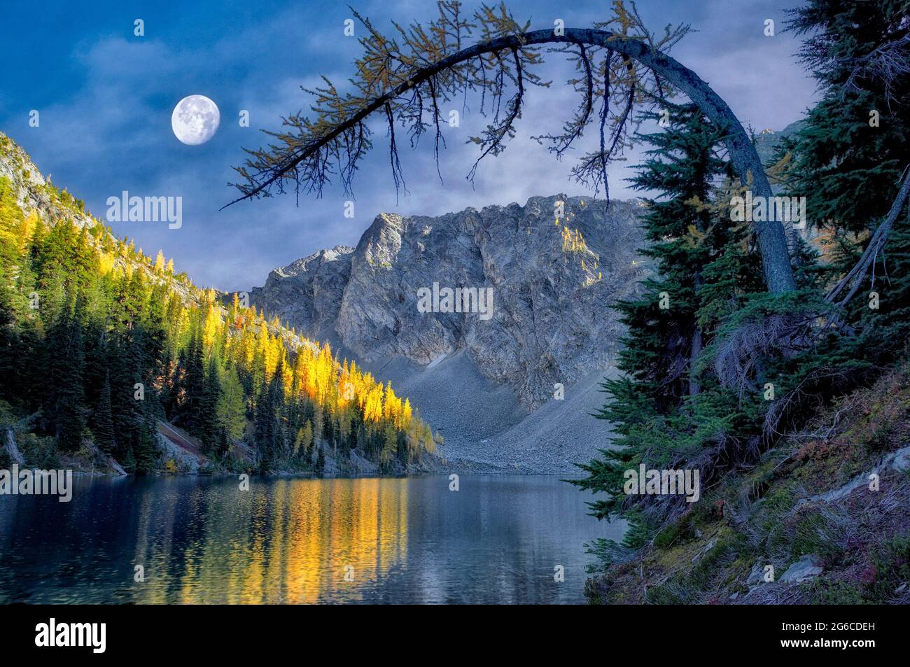 Blue Lake mit Tamarack- oder Lärchenbäumen, die sich in Herbstfarbe und Mond spiegeln. North Cascades National Park. Washington. mond wurde hinzugefügt Stockfoto
