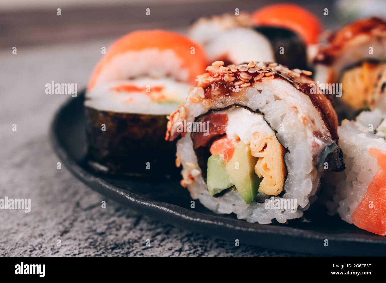 Nahaufnahme von Sushi-Rollen mit Lachs, Avocado und gesmoktem Aal auf dem Betontisch-Hintergrund - Futomaki. Uramaki, hosomaki. Bestellen Sie Lebensmittel online und Stockfoto
