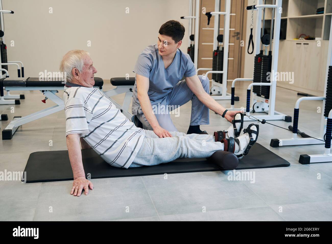 Rentner legt seine Beine auf die Rolle, während Orthopäde Anweisungen gibt Stockfoto