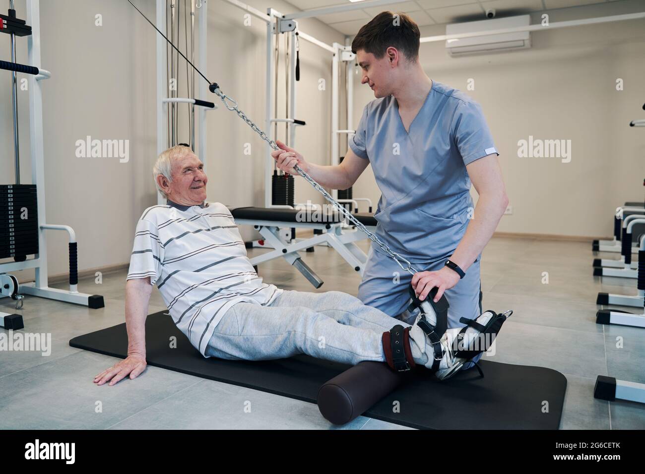 Alter Patient lächelt während der Aktivität des Riemenscheibengewichts den Arzt an Stockfoto