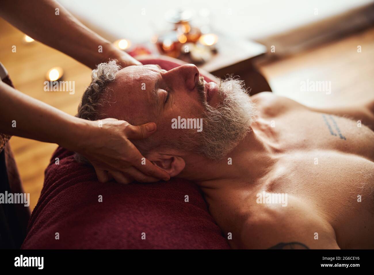 Hübscher grizzled Mann genießt Kopf Massage drinnen Stockfoto