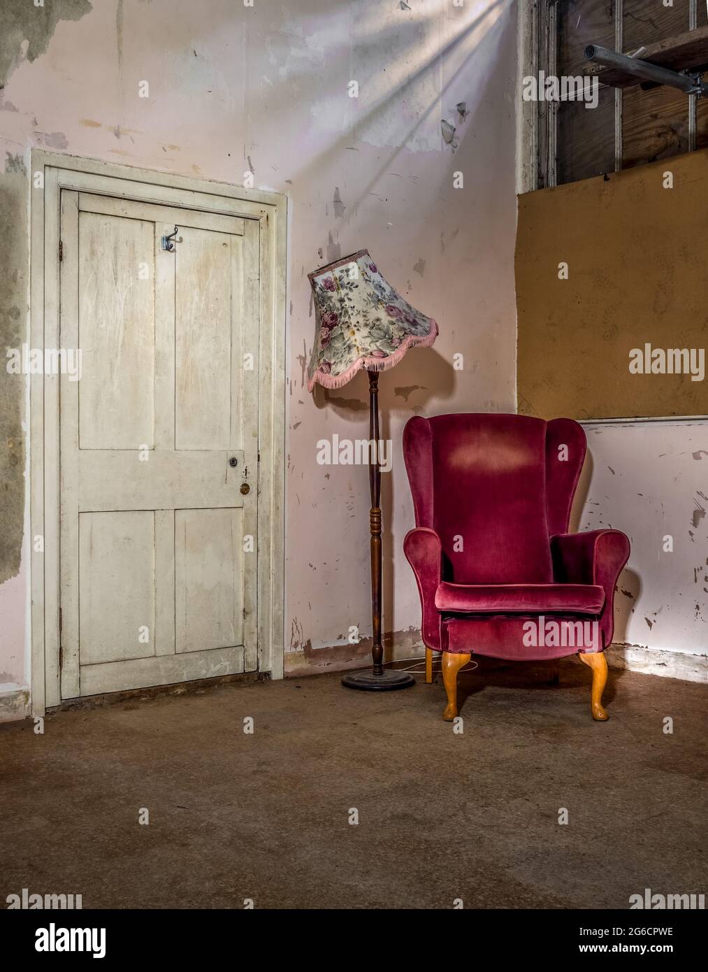 Leerer Stuhl in verwahrlossenem alten Haus mit Lampe und Tür, Lichtkessel. Stockfoto