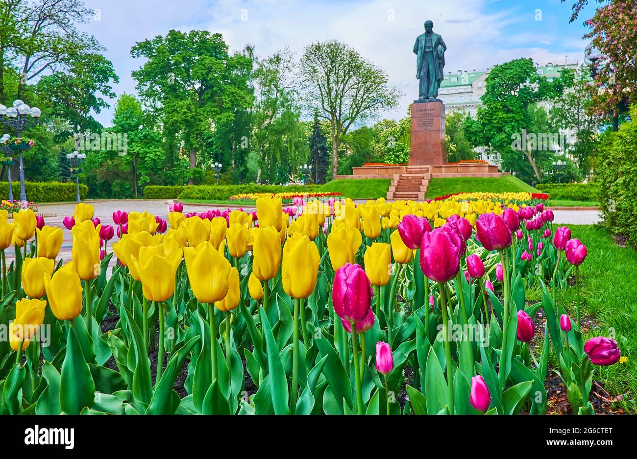 Die Gasse des Taras Shevchenko Parks, gesäumt von blühenden Tulpenblüten, beschnittenen Büschen und üppig grünen Bäumen, ist das Denkmal für Shevchenko zu sehen Stockfoto