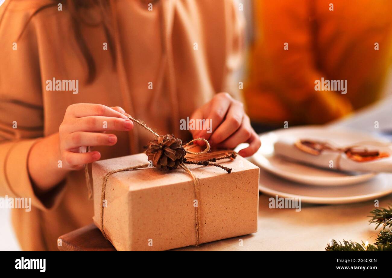 Crop Frau in lässigem Outfit mit Weihnachts-Geschenkbox, während sie am Tisch mit heller Girlande geschmückt sitzt Stockfoto