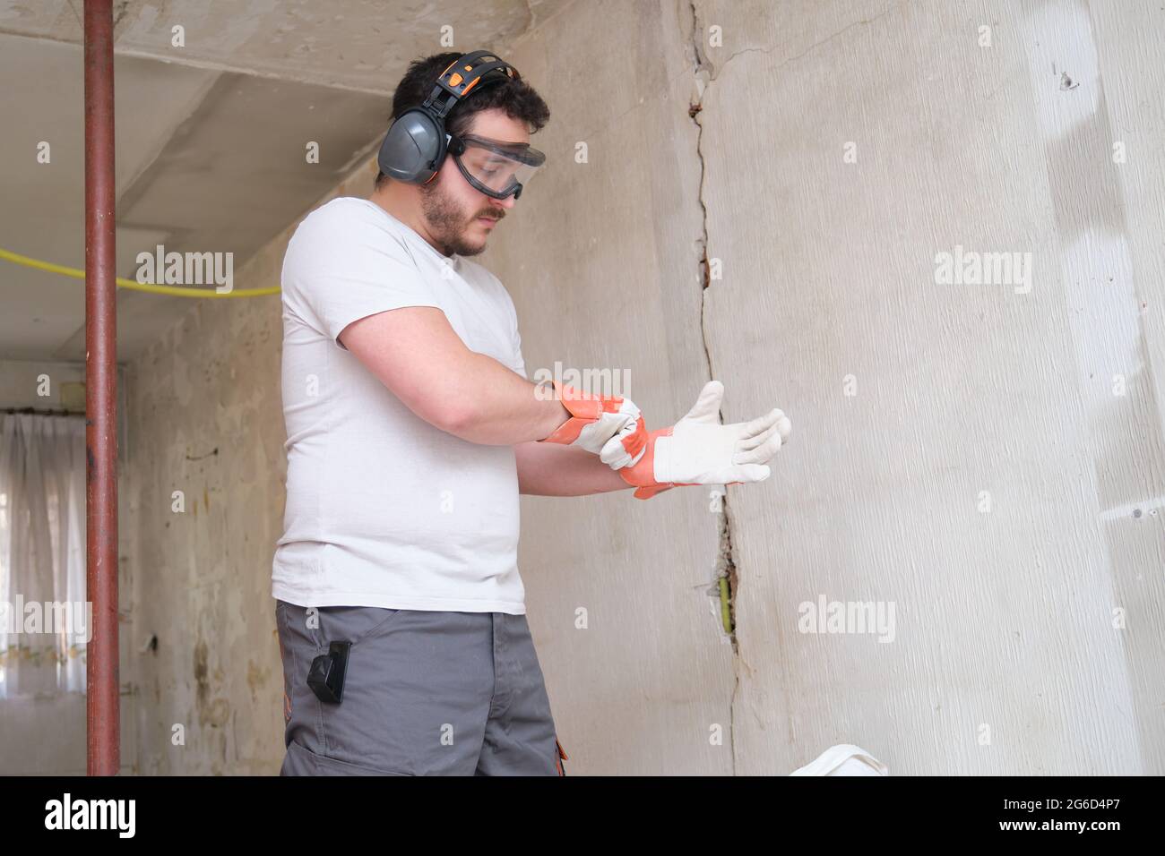 Der Baumeister legt Schutzhandschuhe an, trägt eine Schutzbrille und einen Gehörschutz. Sicherheit am Arbeitsplatz. Stockfoto