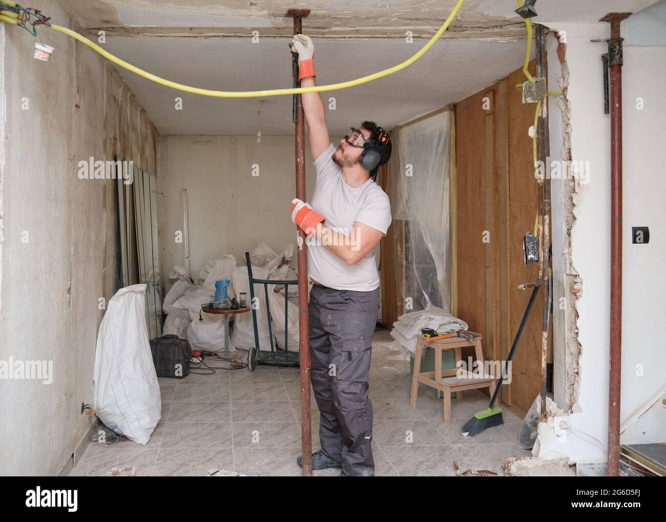 Bauarbeiter, der die erste Säule, Stütze oder Strebe platziert, um einen Einsturz zu verhindern. Der Baumeister trägt Schutzhandschuhe, eine Brille und einen Ohrenschützer. Stockfoto