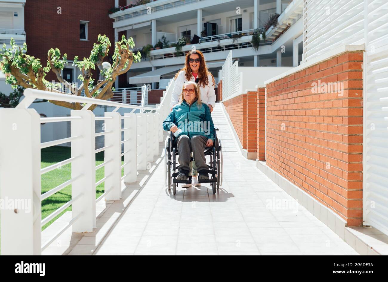 Glückliche Erwachsene Tochter schieben Rollstuhl mit älteren Mutter, während Spaziergang am sonnigen Tag genießen Stockfoto