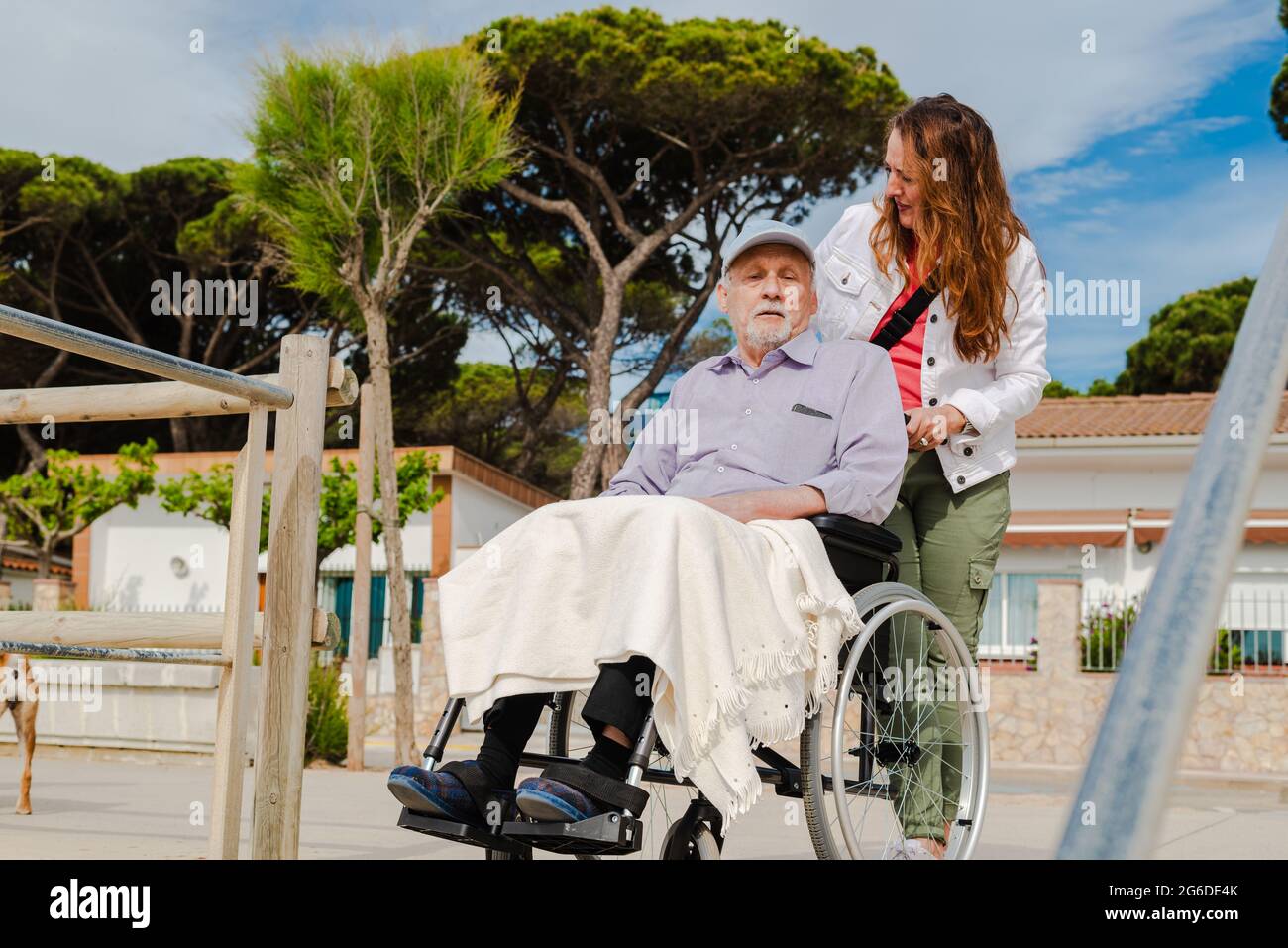 Lächelnde Erwachsene Frau und älterer Mann im Rollstuhl, die sich an sonnigen Tagen in der Stadt entspannen Stockfoto