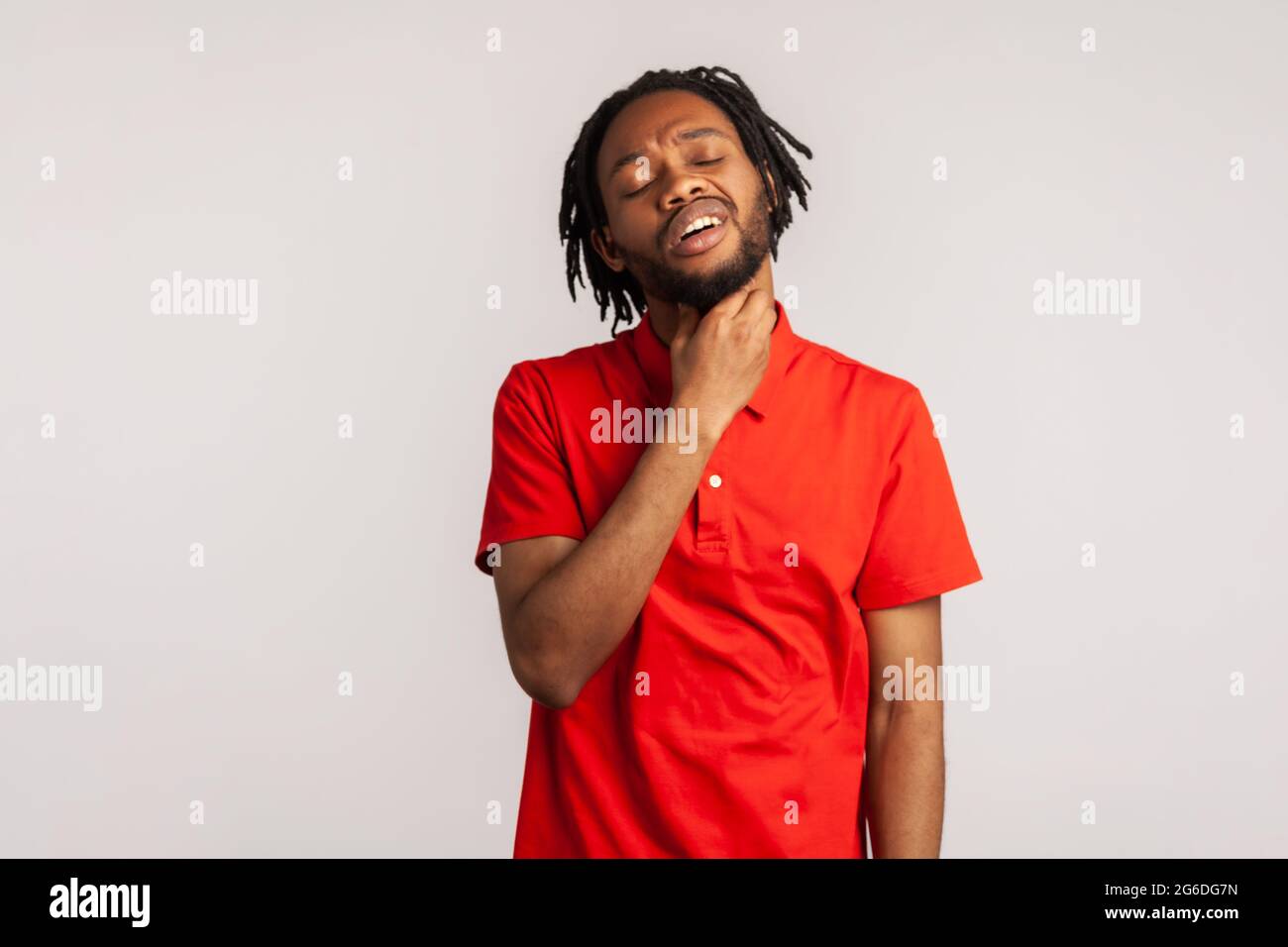 Porträt eines bärtigen Mannes mit Dreadlocks, das ein rotes T-Shirt im Casual-Stil trägt, schmerzhaften Hals berührt, Halsschmerzen, Viren oder Tonsillitis leidet. Innen s Stockfoto