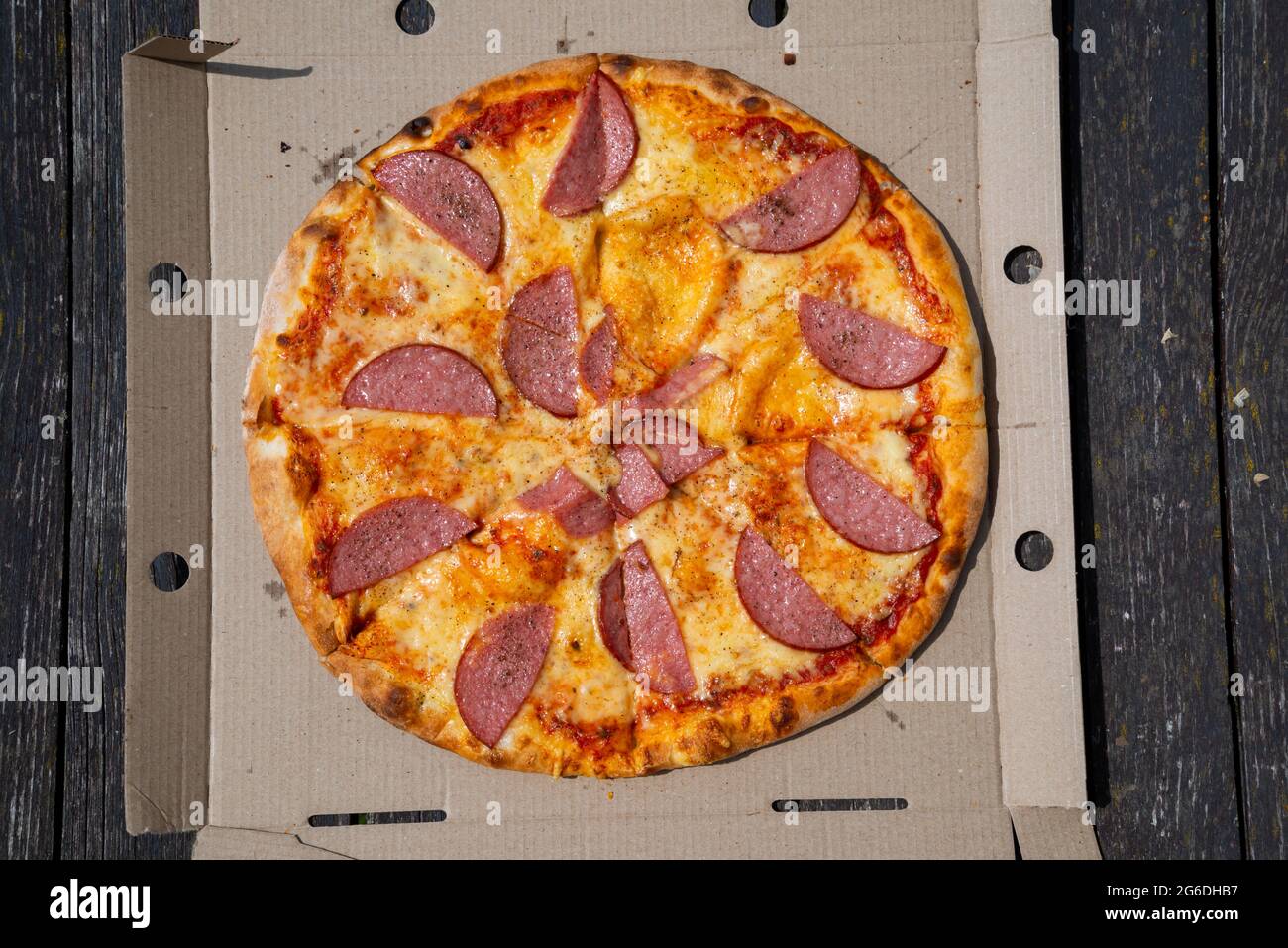 Pizza in einer Pappschachtel vor dunklem Hintergrund. Leerzeichen für Text. Blick von oben. Pizzalieferung. Pizza-Menü. Stockfoto