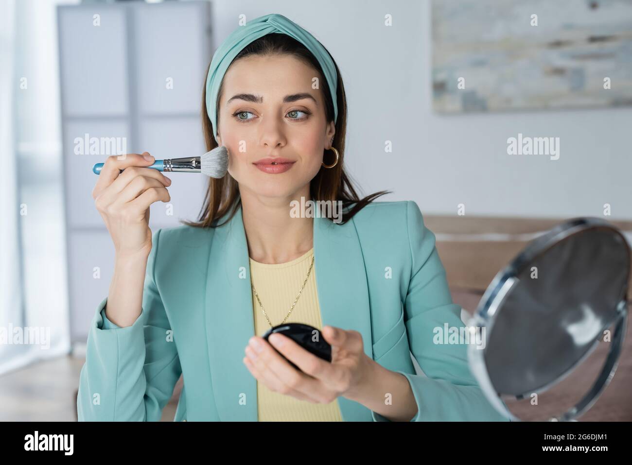 Stilvolle Frau, die Gesichtspuder mit kosmetischen Pinsel in der Nähe verschwommener Spiegel Stockfoto