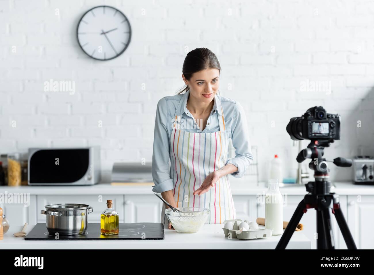 Junge Hausfrau zeigt während des Online-Kochens auf Schüssel mit Mehl in der Nähe der Digitalkamera Stockfoto