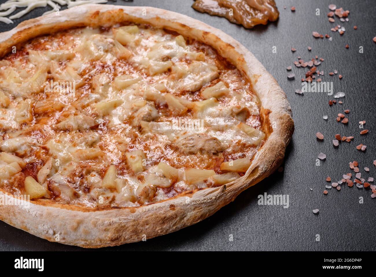 Frische leckere italienische Pizza mit Huhn, Tomaten und Ananas auf dunklem Beton. Italienische Küche Stockfoto