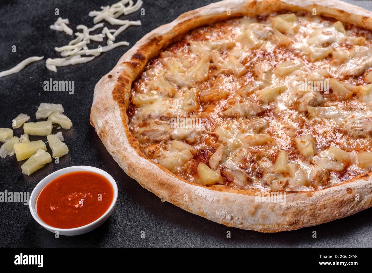 Frische leckere italienische Pizza mit Huhn, Tomaten und Ananas auf dunklem Beton. Italienische Küche Stockfoto