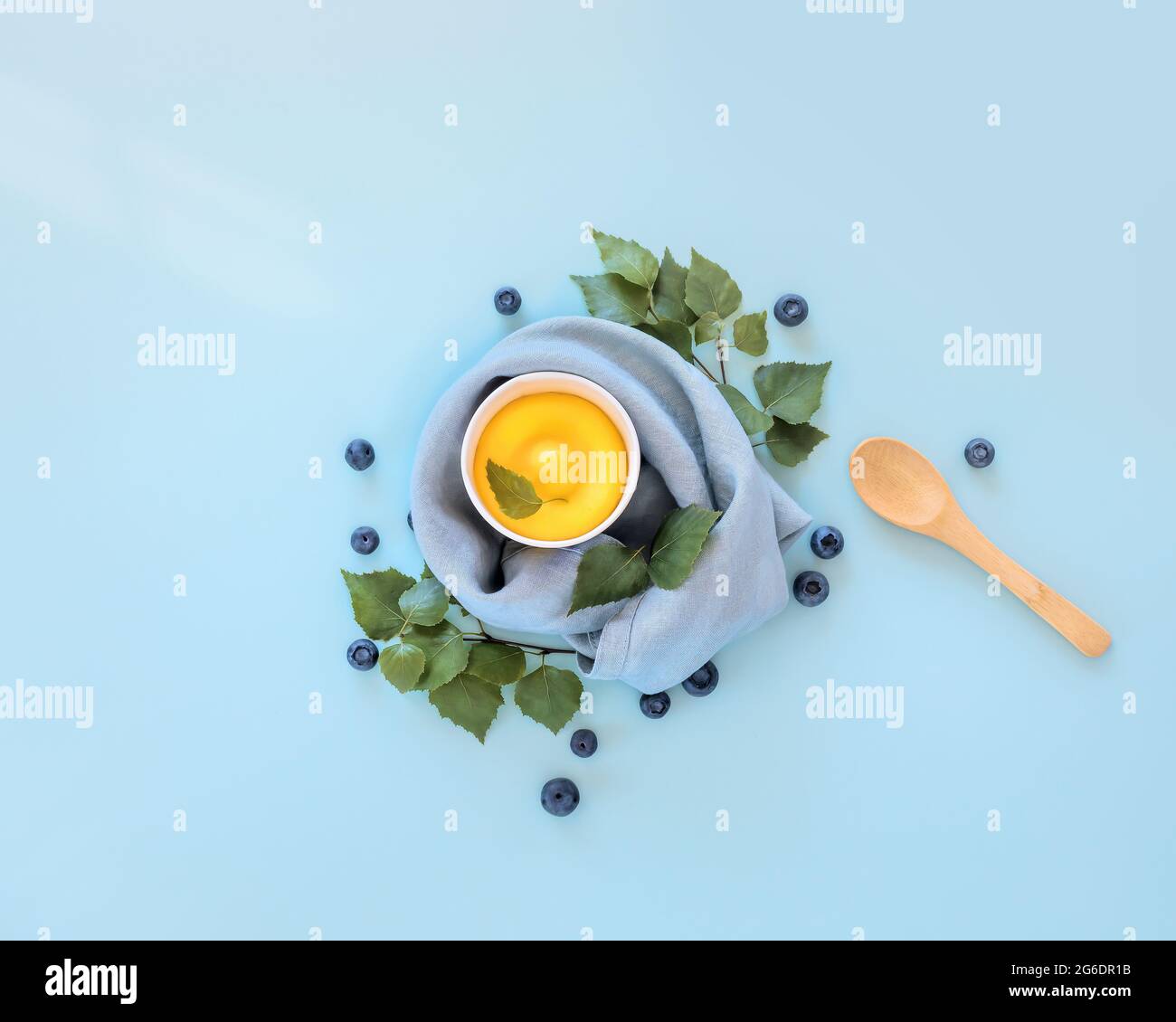 Sommer, umweltfreundlich, Lebensmittelkomposition mit gelbem, hausgemachtem Fruchteis, Heidelbeeren und einem Holzlöffel auf blauem Hintergrund. Veganes Eis Stockfoto