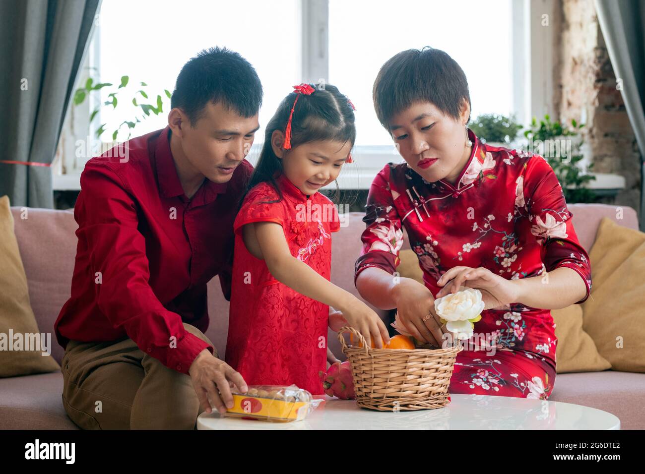 Kleines chinesisches Mädchen in rotem Kleid hilft Eltern Snack in den Korb zu legen Stockfoto