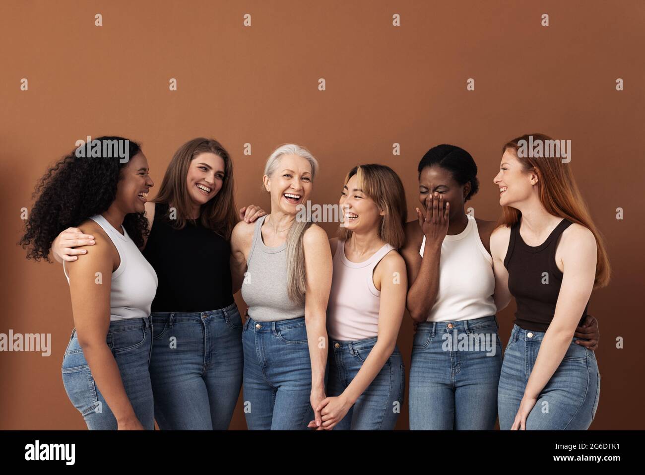 Stilvolle Frauen unterschiedlichen Alters haben Spaß beim Tragen von Jeans und Unterhemden auf braunem Hintergrund Stockfoto