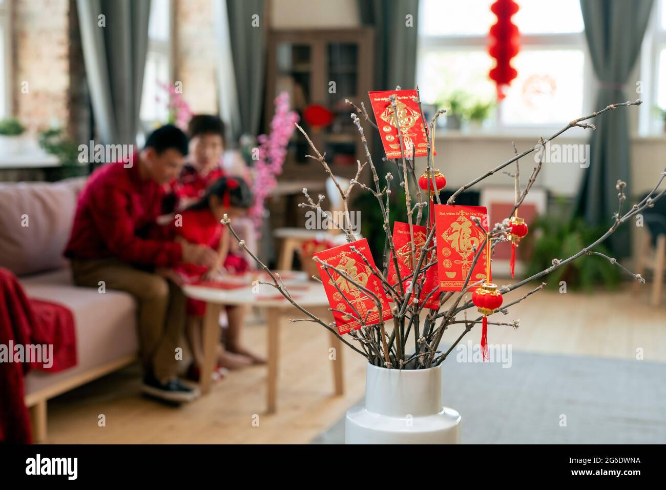 Rote chinesische Neujahrspostkarten und Laternen hängen an trockenen Zweigen in weißer Vase Stockfoto