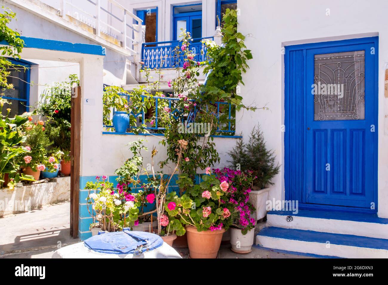 Plaka Town auf der Insel Milos - malerische schmale Steinstraße mit traditionellen griechischen weiß getünchten Wänden, blauen Türen, Fensterläden und blühenden Blumen. Stockfoto