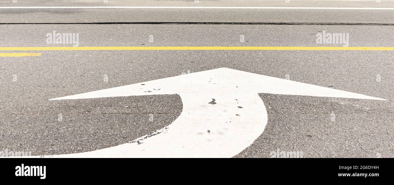 Großer weißer Richtungspfeil auf der Straße, der eine Linksabbiegung signalisiert Stockfoto