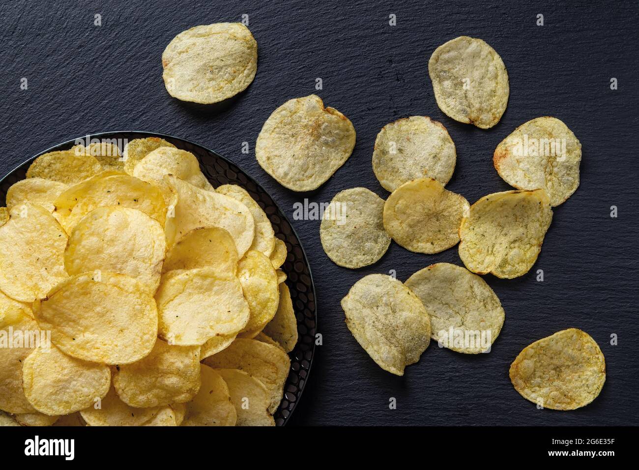 Draufsicht auf knusprige Kartoffelchips auf einer schwarzen Keramikplatte über schwarzer Oberfläche. Leckerer Snack aus frittierten dünnen Kartoffelscheiben. Bereit, Fastfood zu essen. Stockfoto