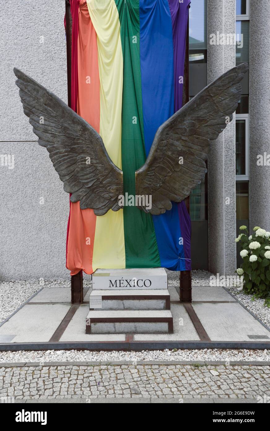 Ein Paar Flügel als Skulptur, dahinter die Regenbogenfahne an der Außenwand der mexikanischen Botschaft, Berlin, Deutschland Stockfoto