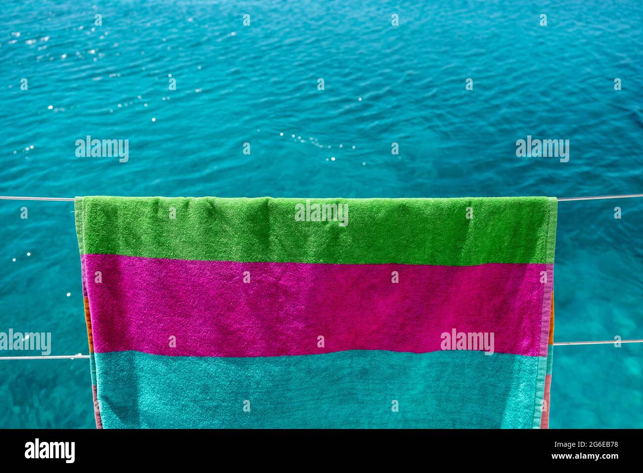 Strandtuch trocknen auf Wäscheleine, verwischen Meereshintergrund. Buntes Handtuch, das an der Edelstahlschiene des Bootes hängt. Sommerferien und Segeln, Wäsche waschen und Stockfoto