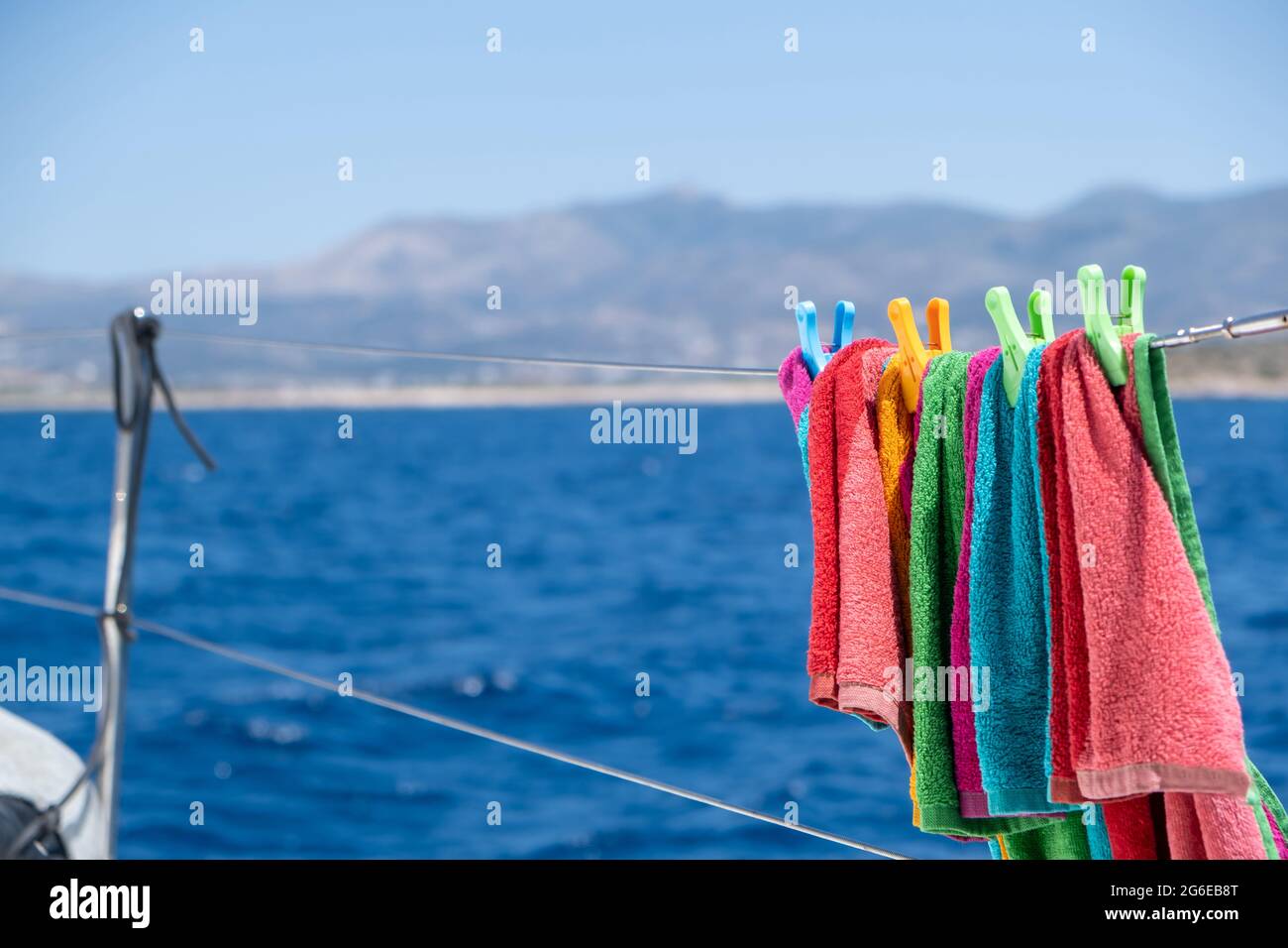 Strandtuch trocknen auf Wäscheleine, verwischen Meereshintergrund. Buntes Handtuch, das an der Edelstahlschiene des Bootes hängt. Sommerferien und Segeln, Wäsche waschen und Stockfoto