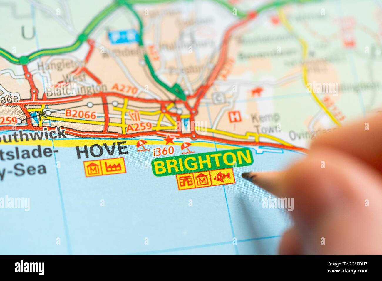 Nahaufnahme einer Seite in einem gedruckten Roadmap-Atlas mit einer Männerhand, die einen Bleistift hält und auf den Badeort Brighton am Ärmelkanal zeigt Stockfoto