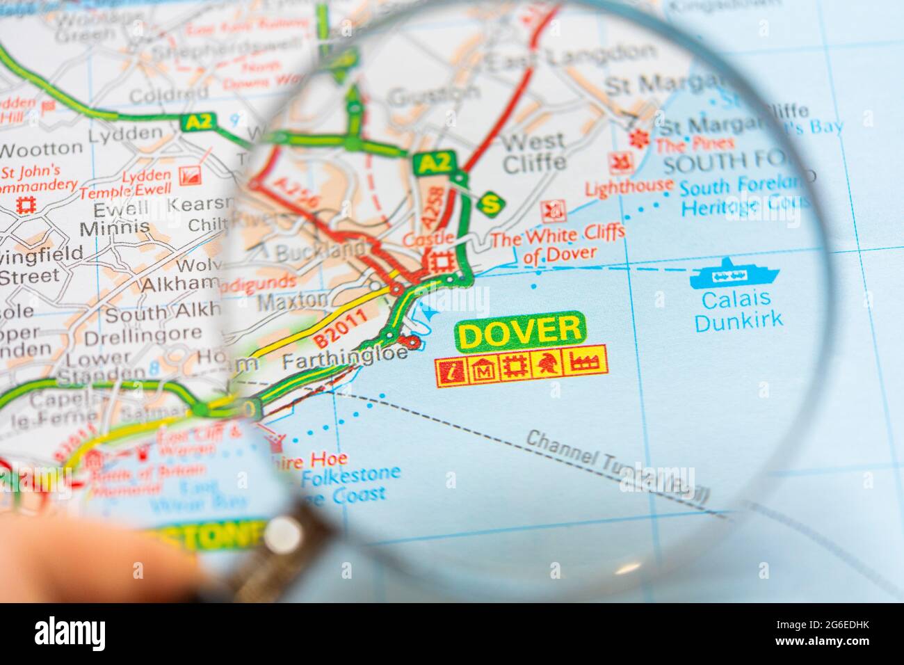 Eine Makroansicht einer Seite in einem gedruckten Roadmap-Atlas mit einer Hand eines Mannes, der eine Lupe hält, die eine Vergrößerung der Stadt in England zeigt Stockfoto