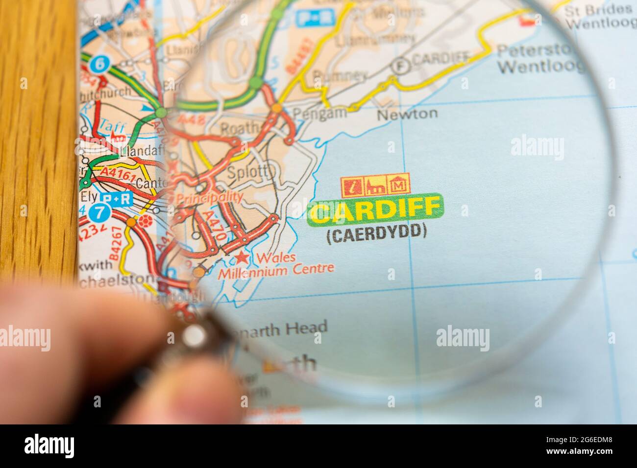 Nahaufnahme einer Seite in einem gedruckten Straßenkarte-Atlas mit einer Männerhand, die eine Lupe mit einer Vergrößerung von Cardiff (Caerdydd) in Wales hält Stockfoto