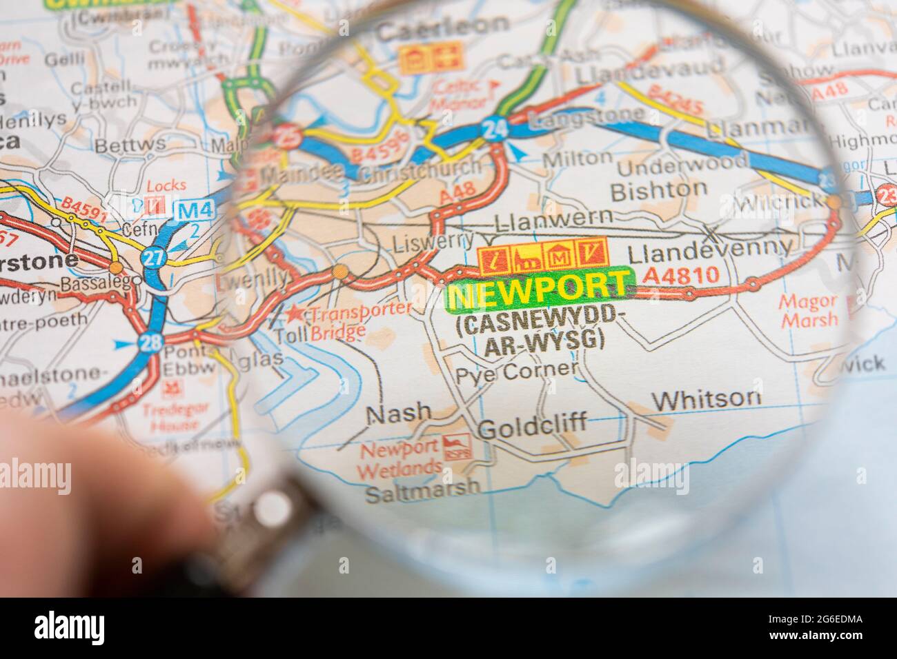 Nahaufnahme einer Seite in einem gedruckten Straßenkarte-Atlas mit einer Männerhand, die eine Lupe mit einer Vergrößerung der walisischen Stadt Newport hält Stockfoto